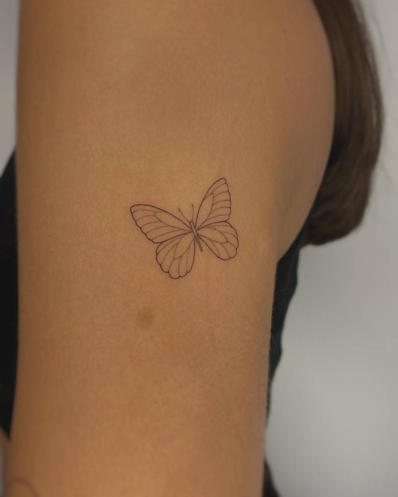 Little butterfly tattoo in fine line style located on the upper arm.