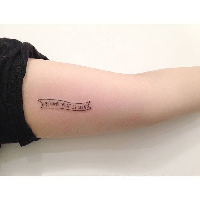 "Beyond what is seen" banner tattoo located on the inner arm.