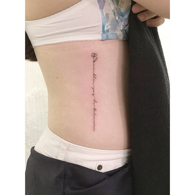 Fine line style flower and handwritten lettering tattoo located on the rib.