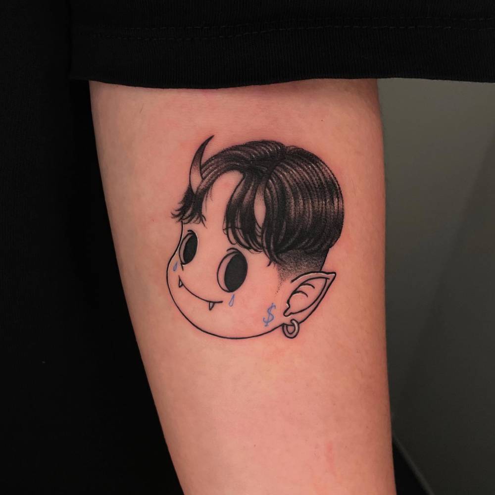Cartoon style cute devil portrait tattoo located on the inner forearm.