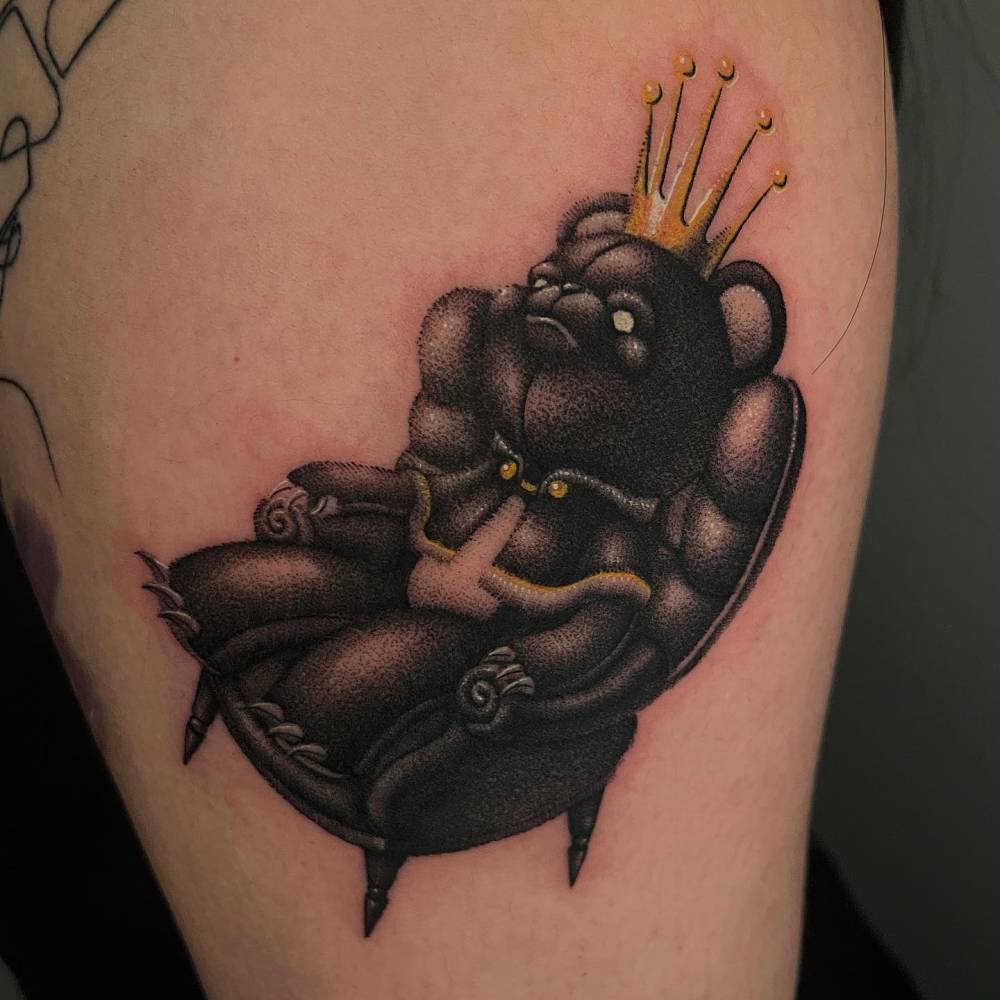 King teddy bear tattoo in dotwork style placed on the upper arm.