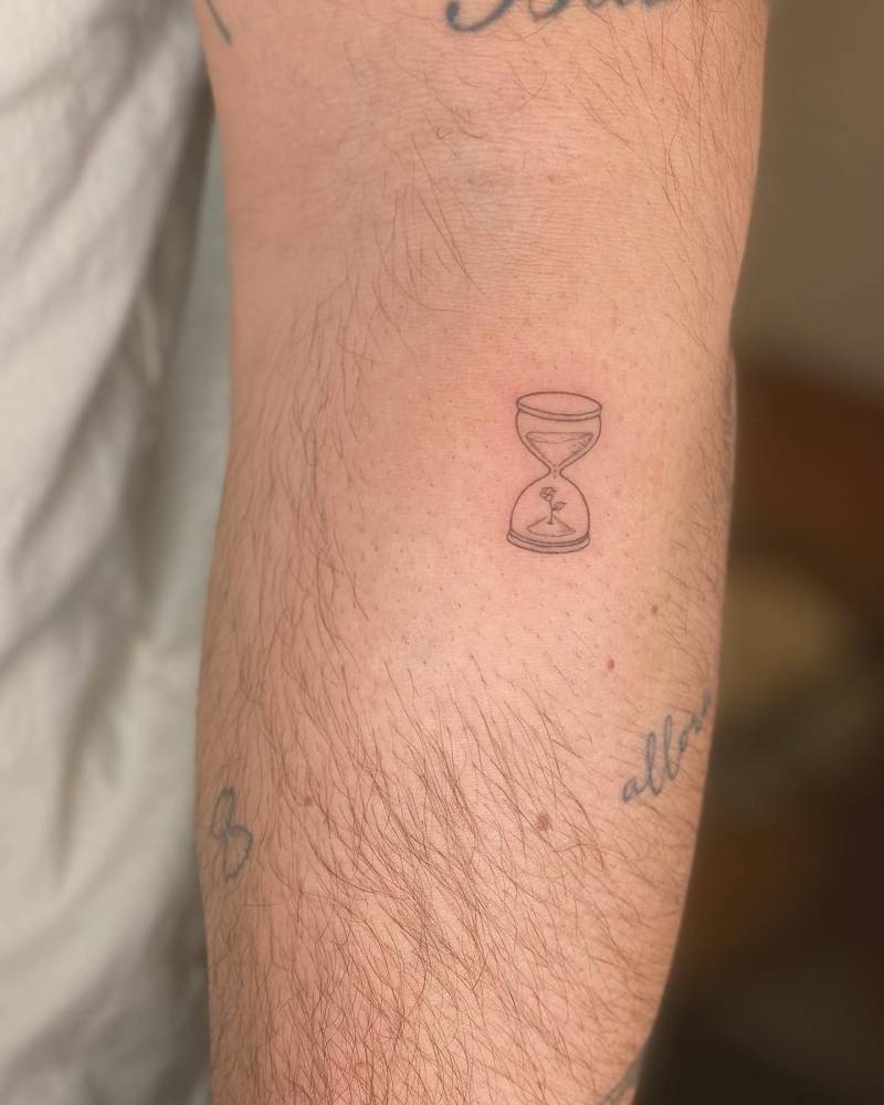 Hourglass and flower tattoo in fine line style located on the forearm.