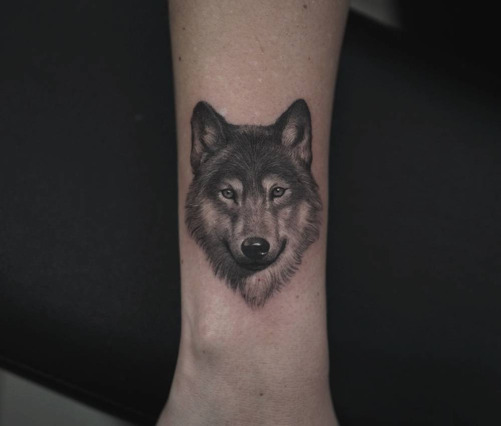 Wolf portrait tattoo located on the wrist, done in micro-realistic style.