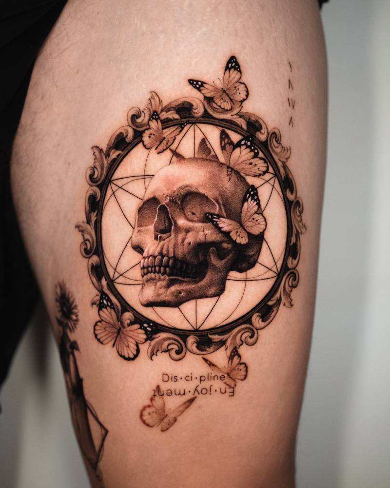 Skull and frame tattoo in micro-realistic style placed on the thigh.