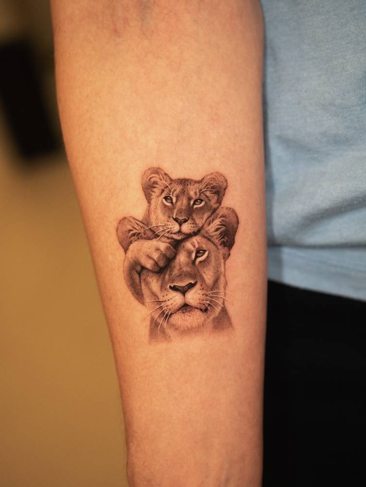 Micro-realistic style lioness and cub tattoo located on the inner forearm.