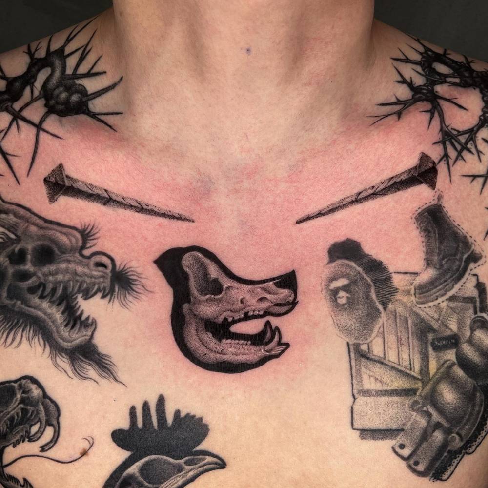 Wolf skull and nails tattooed on the collarbone and chest.