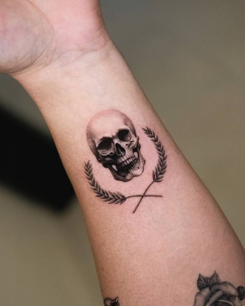 Laurel wreath and skull tattoo in micro-realistic style placed on the wrist.
