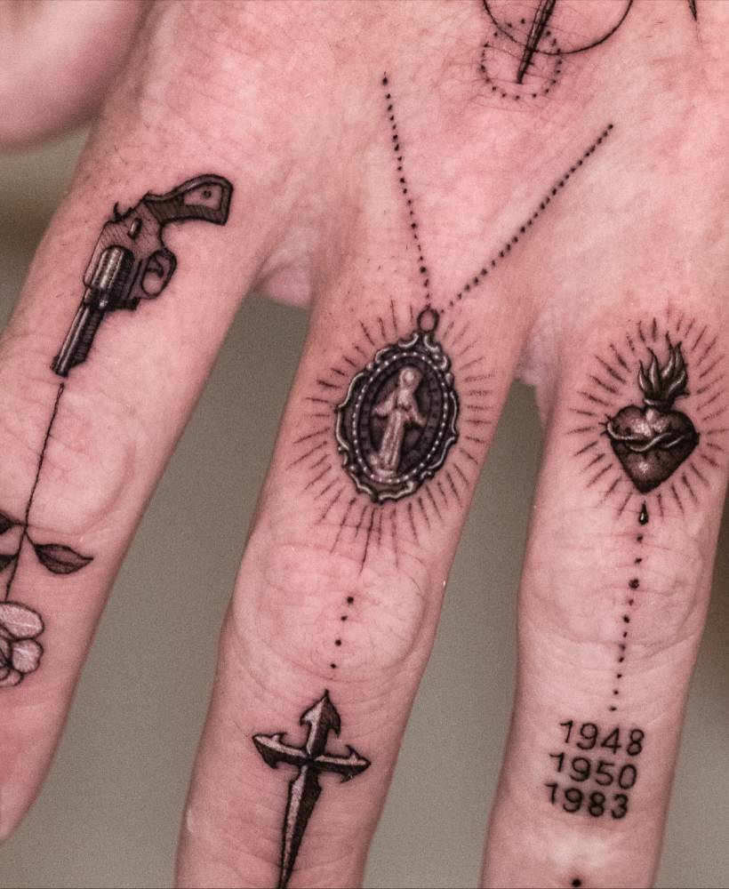 Revolver, pendant and sacred heart tattoos located on the fingers.