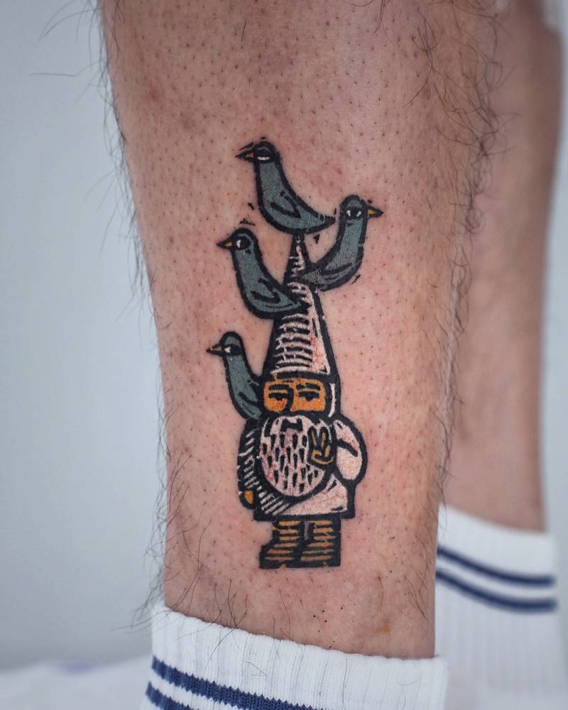 Pop art style gnome and pigeons tattoo located on the shin.