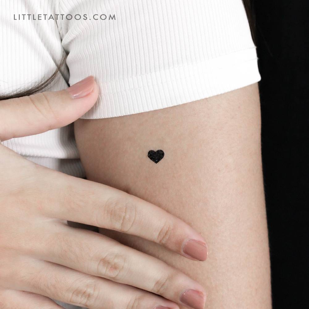 Little minimalistic black heart temporary tattoo located on the upper arm.