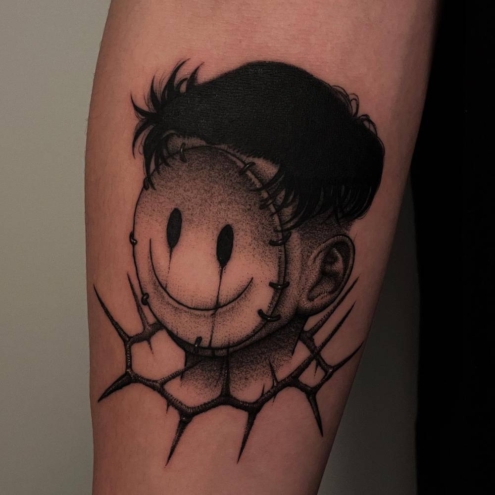 Smiley mask and thorns tattoo located on the inner forearm.