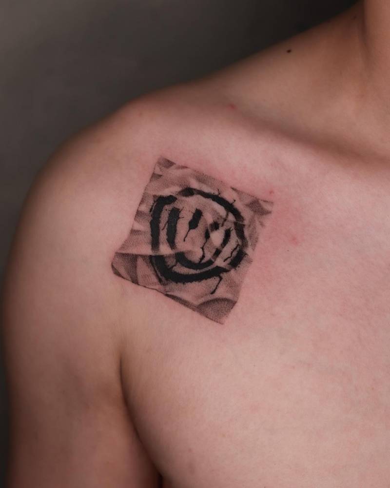 Smiley face piece of paper tattoo located on the shoulder.