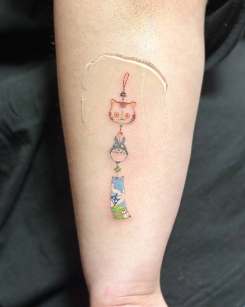 Cartoon style Totoro norigae tattoo located on the forearm.