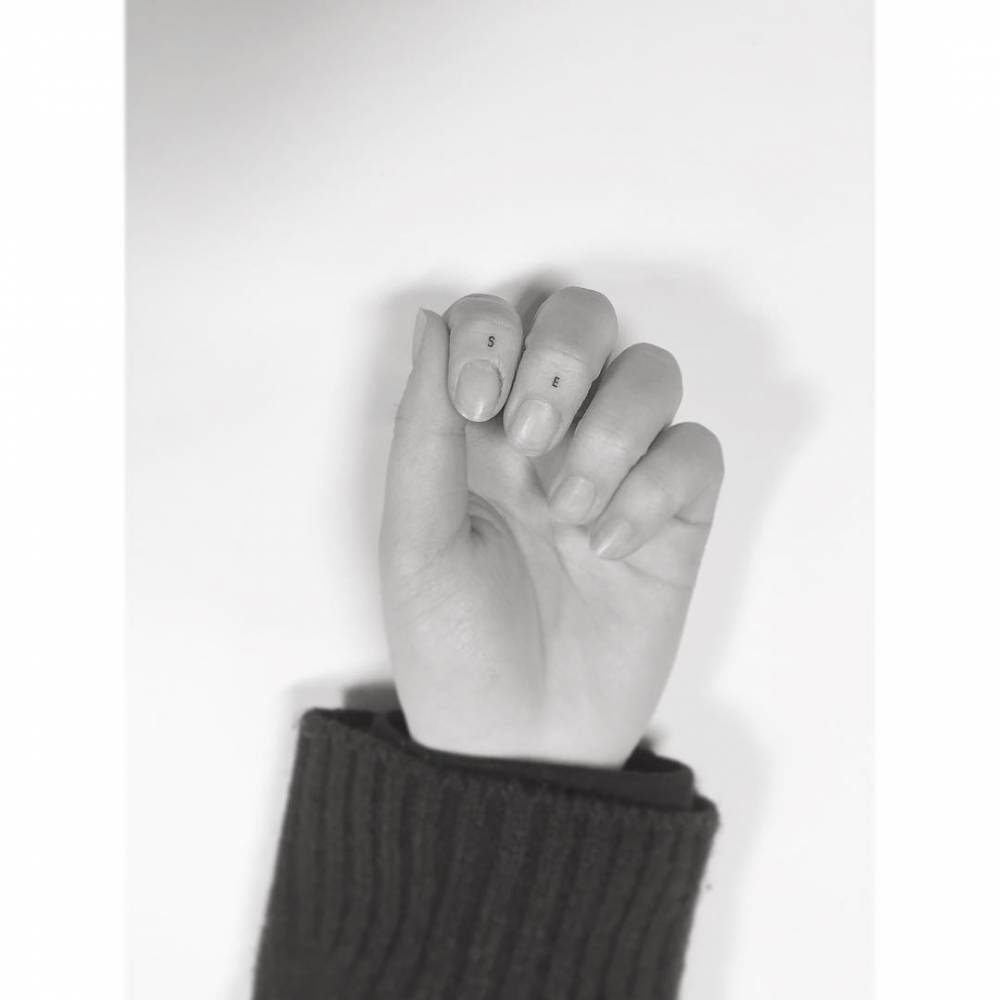 Initials "S" and "E" tattooed on the fingers, minimalistic style.