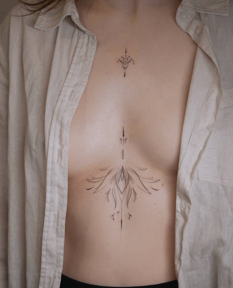 Fine line style ornamental tattoo located on the sternum.