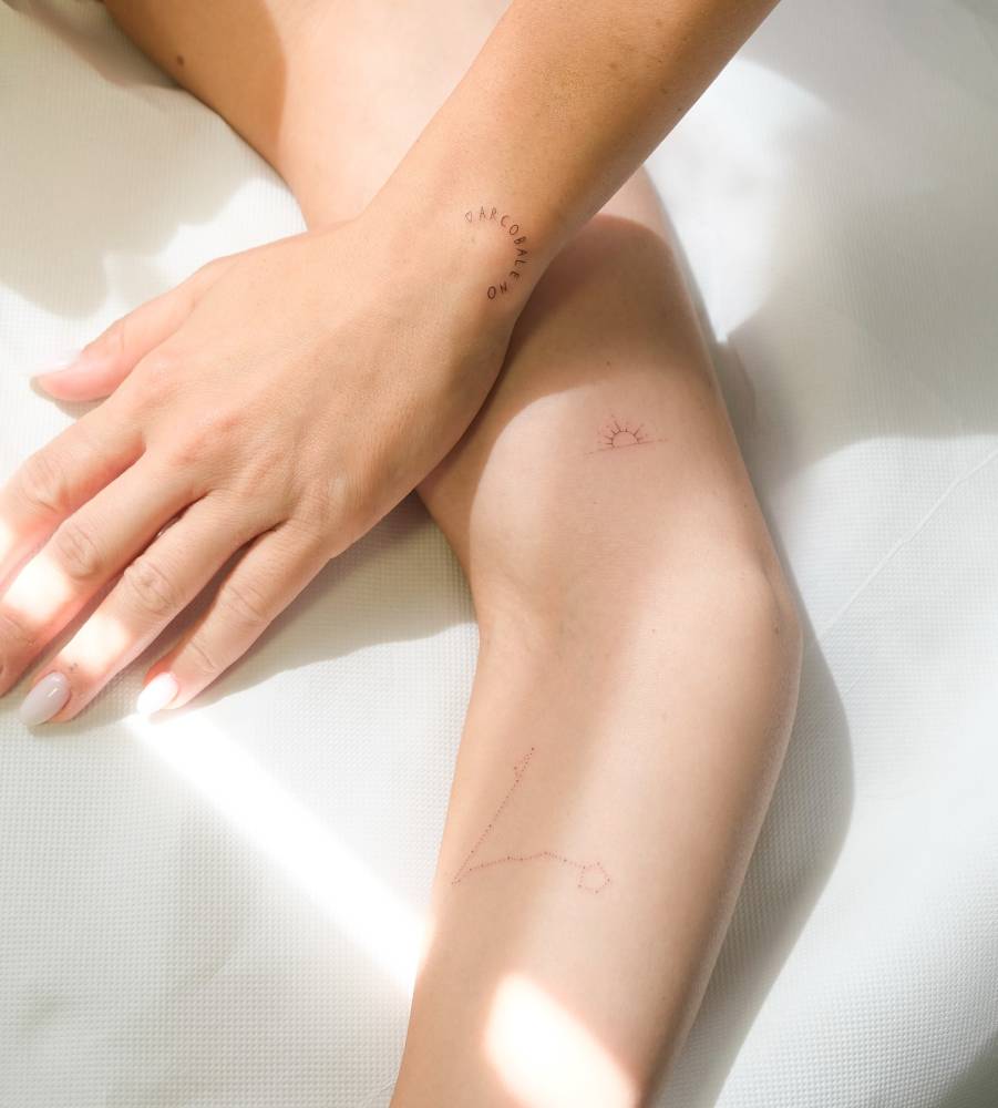 Sunset and Pisces constellation tattoos located on the arm, fine line style.
