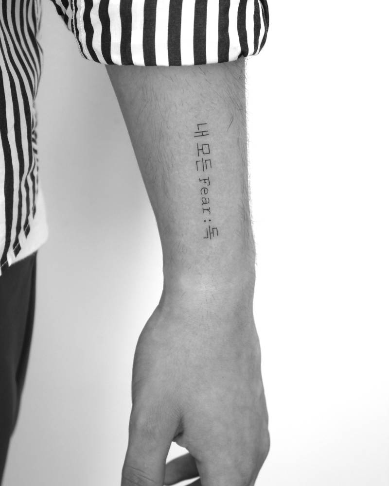 Korean lettering and word "fear" tattooed on the wrist.