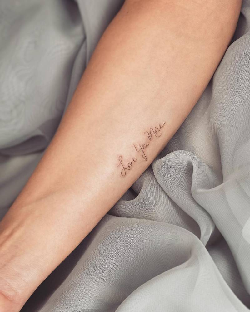 "Love you more" lettering tattoo handwritten on the inner forearm.