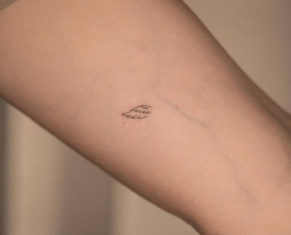 Tiny minimalistic wing tattooed on the inner arm.