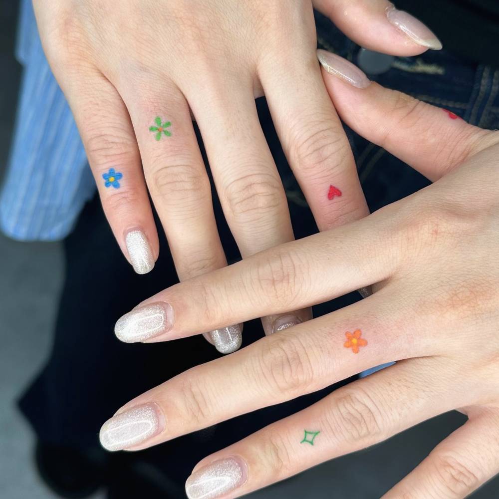 Individual matching hand poked flowers, star and red heart tattoos located on the fingers.