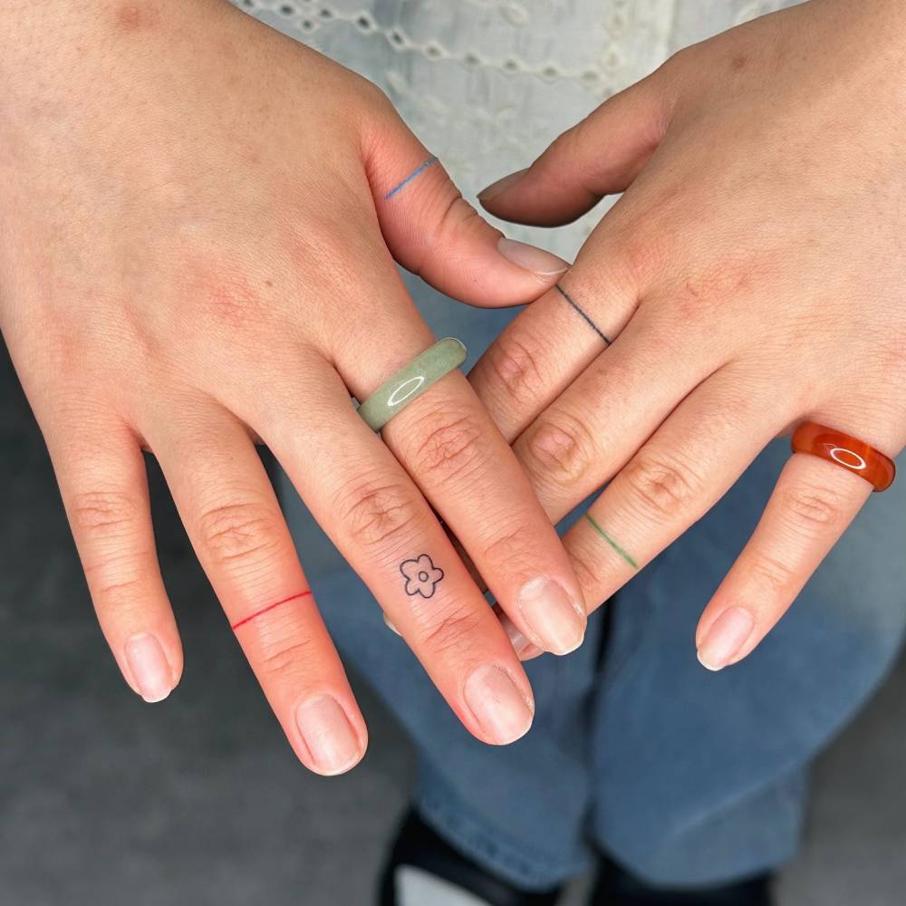 Minimalistic style rings and flower tattoos located on the fingers.