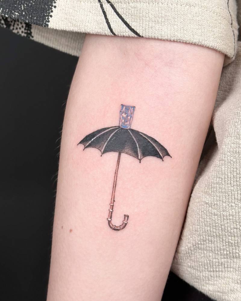 Cartoon style umbrella and glass tattoo located on the inner forearm.