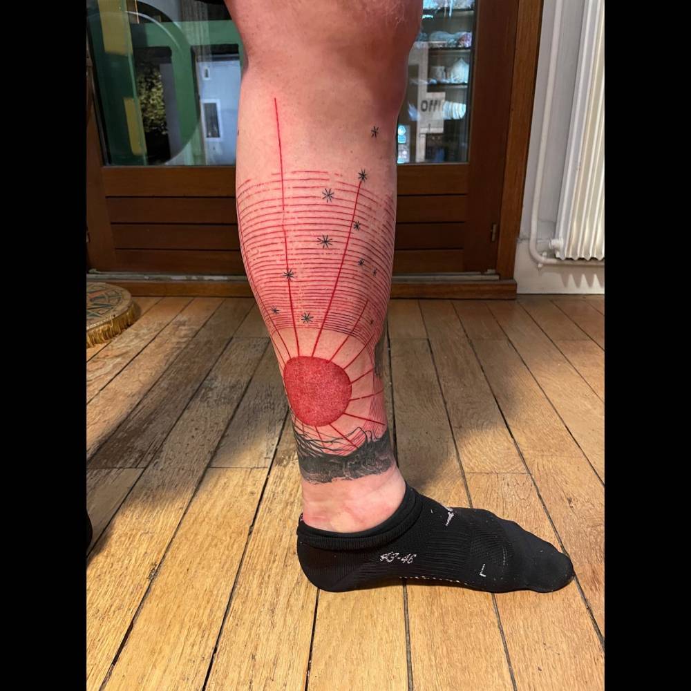 Graphic style red sun tattoo located on the shin.