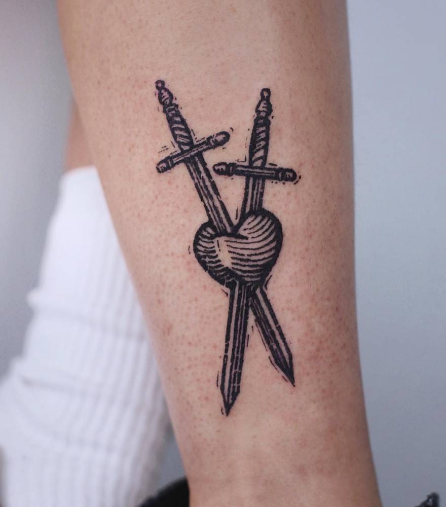 Engraving style heart and swords tattoo located on the shin.
