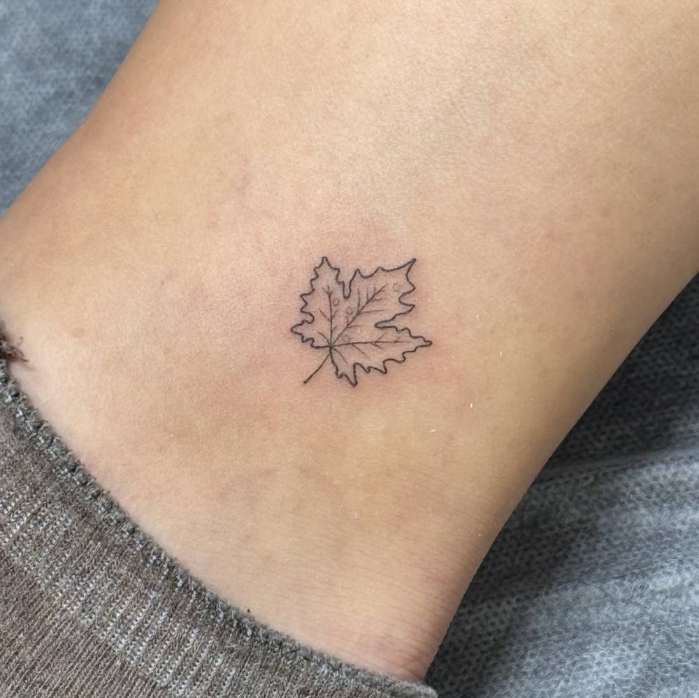 Maple leaf tattoo in fine line style located on the ankle.