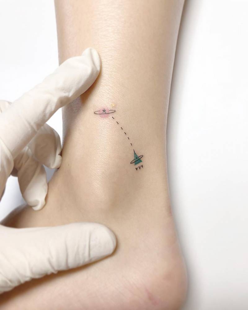 Rocket to Saturn tattooed on the ankle, done in minimalistic style.