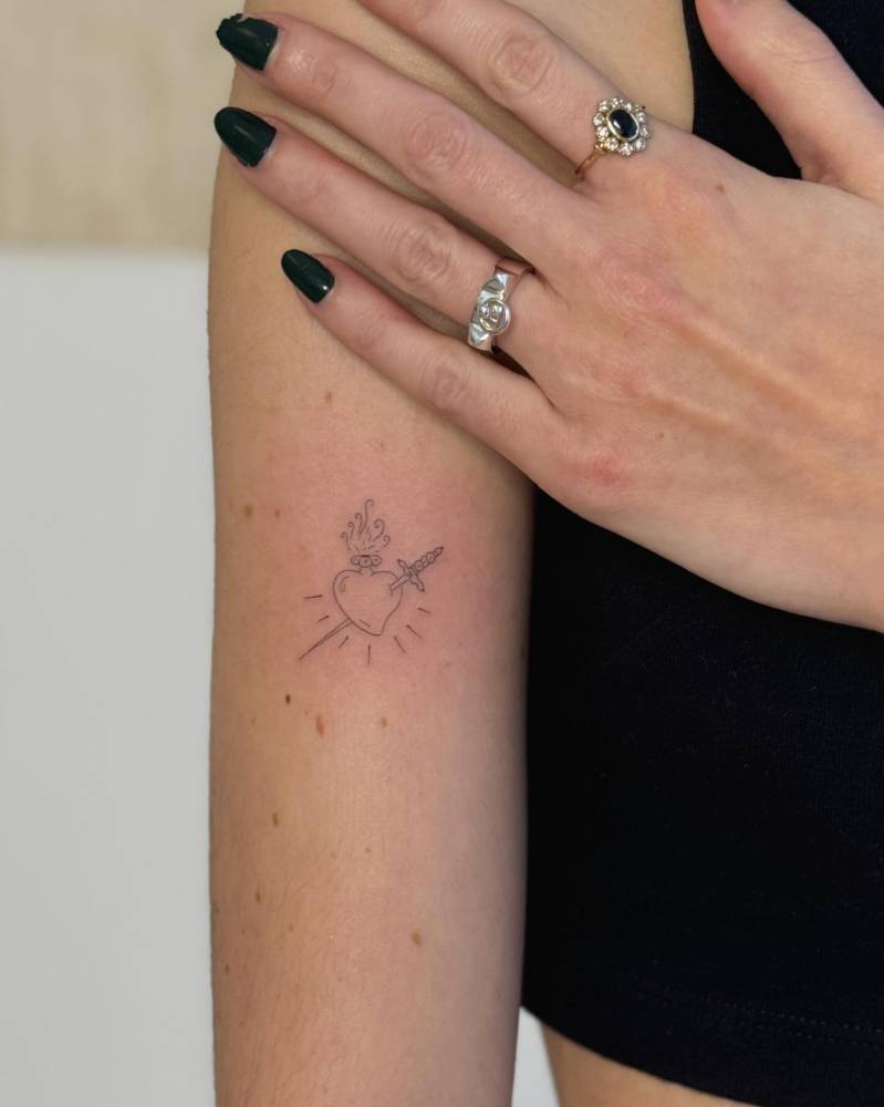 Flaming heart and sword tattoo in fine line style placed on the upper arm.