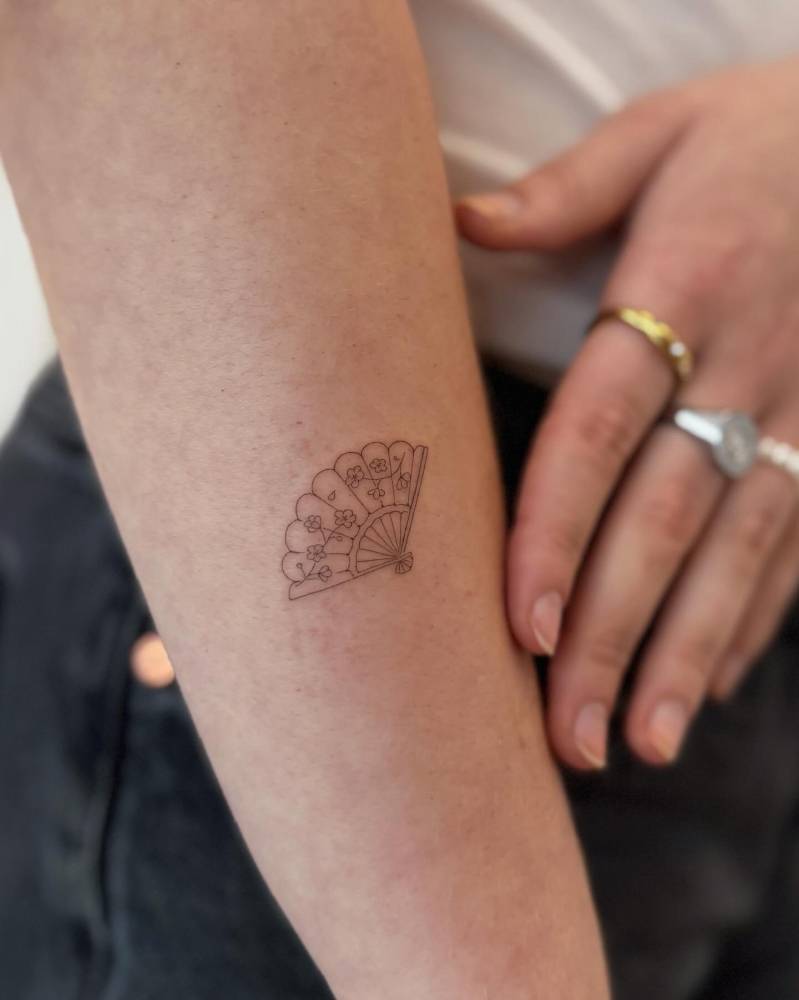 Hand fan tattoo in fine line style placed on the forearm.