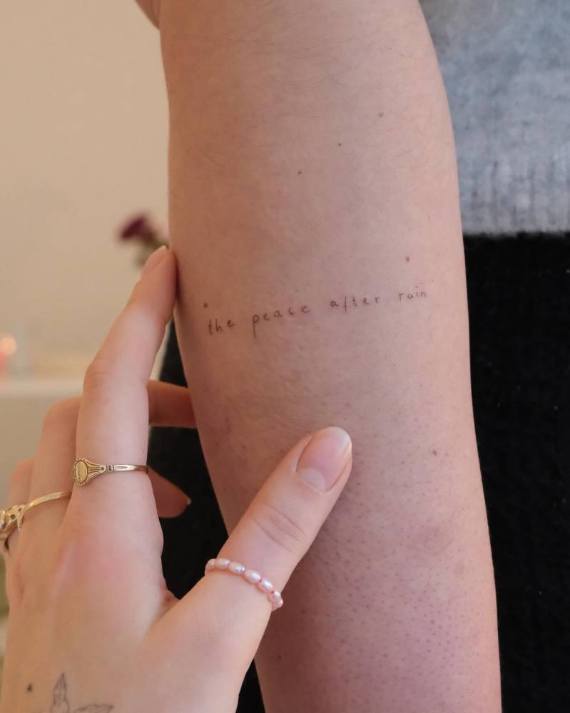 "The peace after rain" lettering tattoo handwritten on the forearm.
