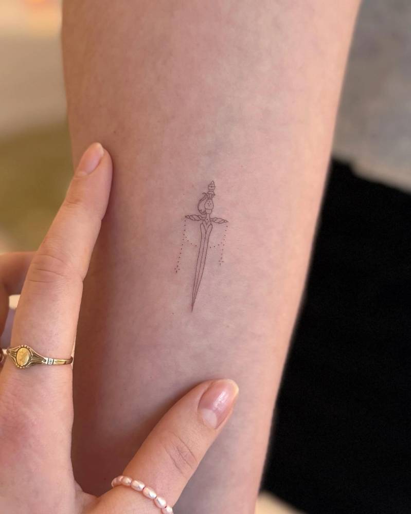 Dagger tattoo in fine line style placed on the inner forearm.