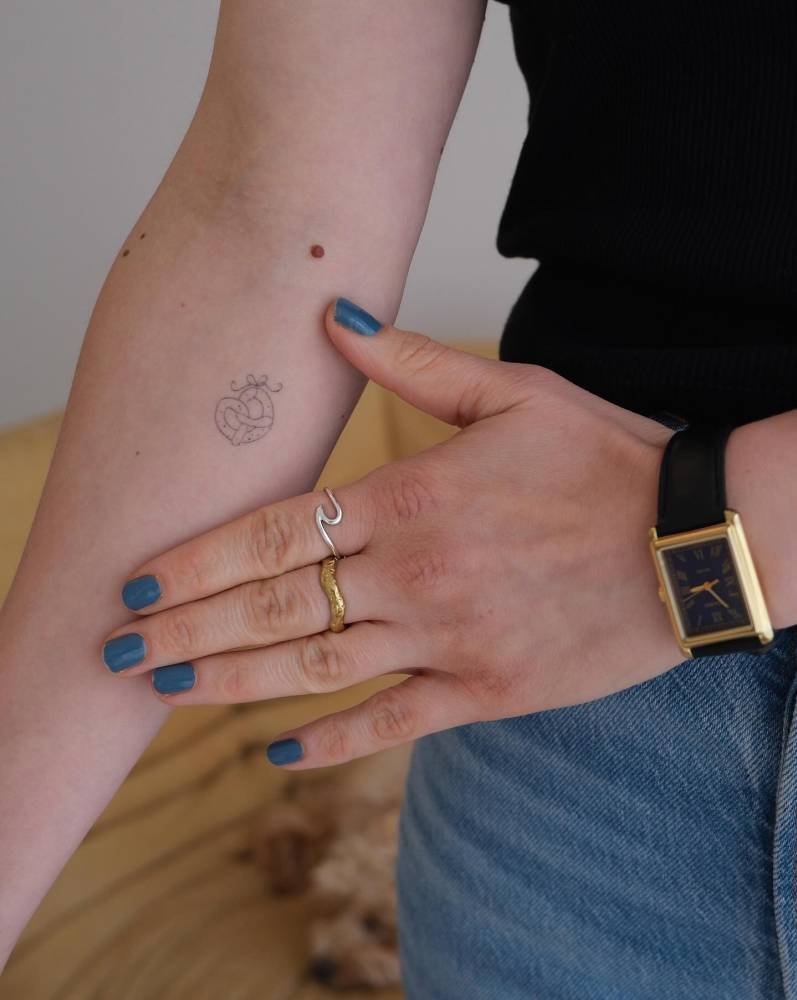 Fine line style pretzel tattoo placed on the inner forearm (healed).