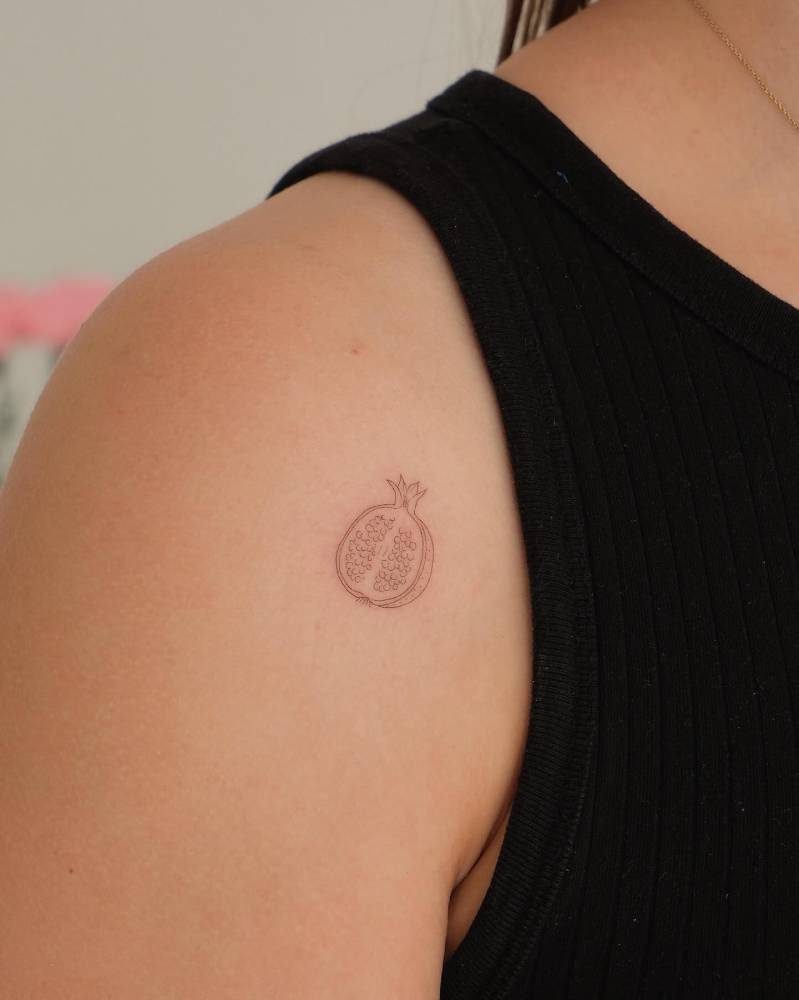 Little pomegranate tattoo in fine line style done on the shoulder.