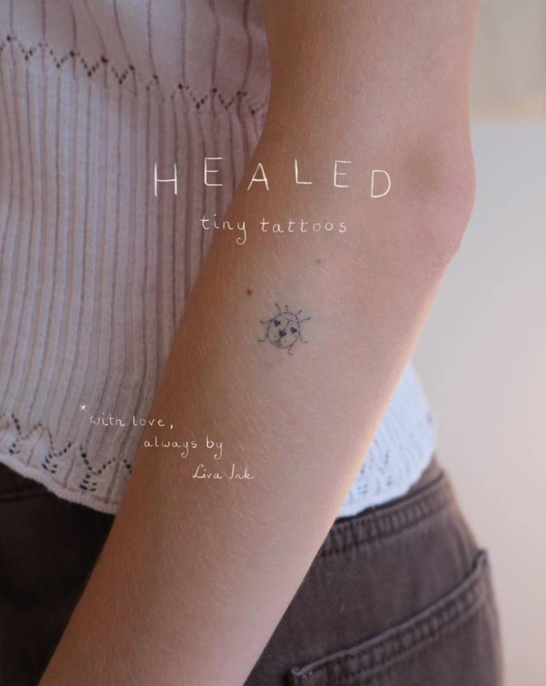 Healed ladybug tattoo in fine line style located on the forearm.