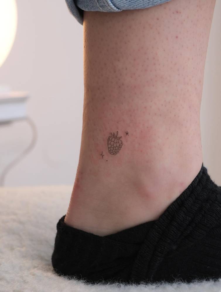 Little raspberry tattoo in fine line style located on the ankle.