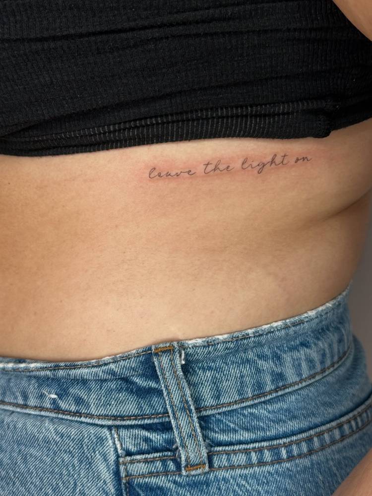 "Leave the light on" lettering tattoo located on the rib.