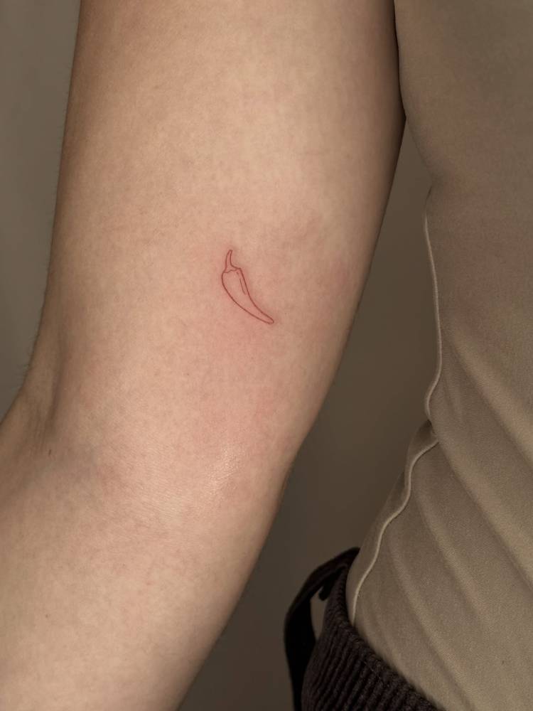 Tiny minimalistic red chili pepper tattoo placed on the inner arm.