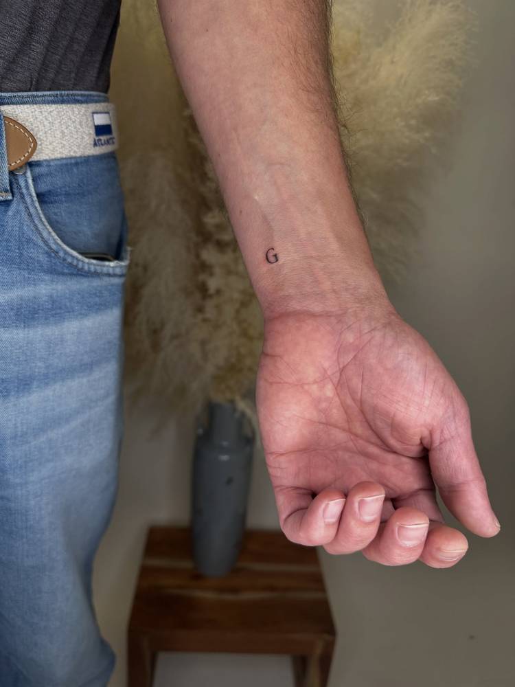 Tiny letter "G" in serif font located on the wrist.