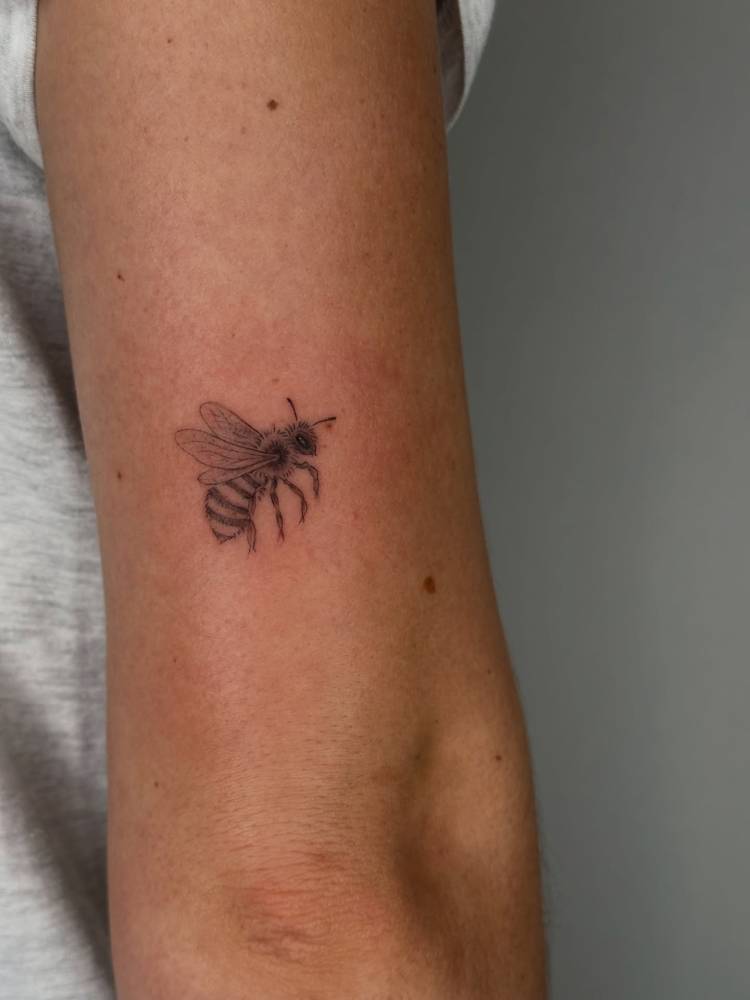 Bee tattoo in illustrative style located on the tricep.