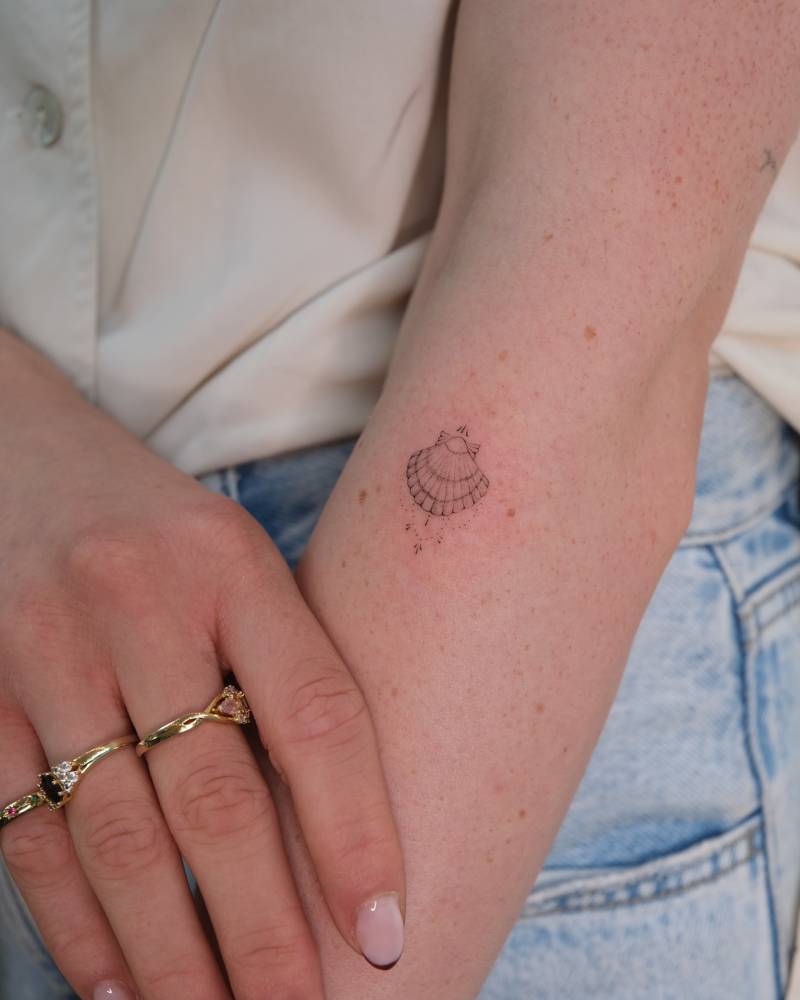 Scallop shell tattoo in fine line style located on the forearm.