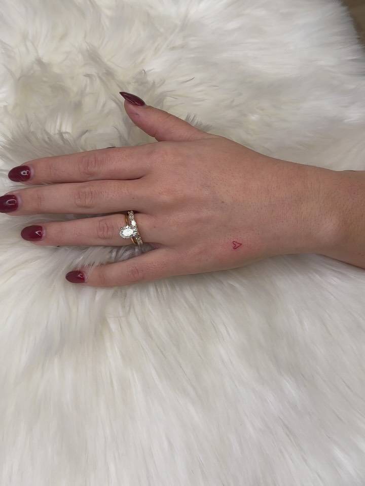 Tiny red heart tattoo located on the hand.