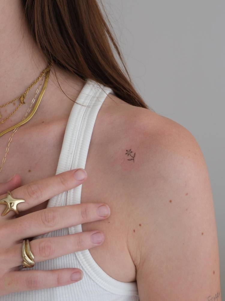 Tiny minimalistic flower tattoo located on the shoulder.
