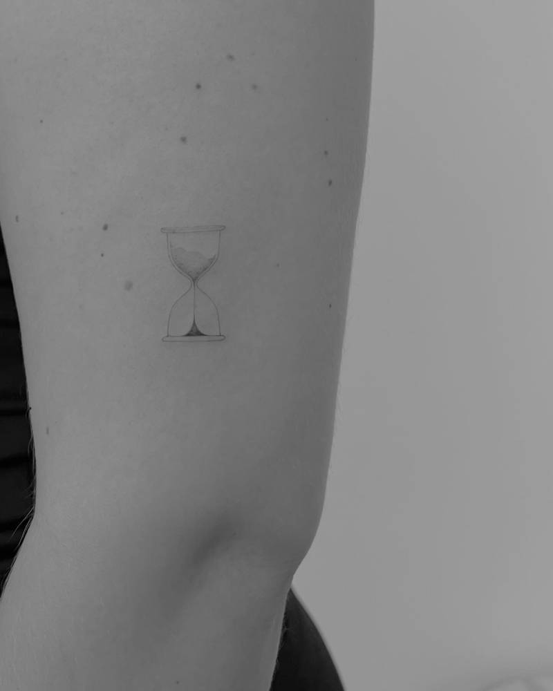 Little hourglass tattoo in fine line style located on the upper arm.