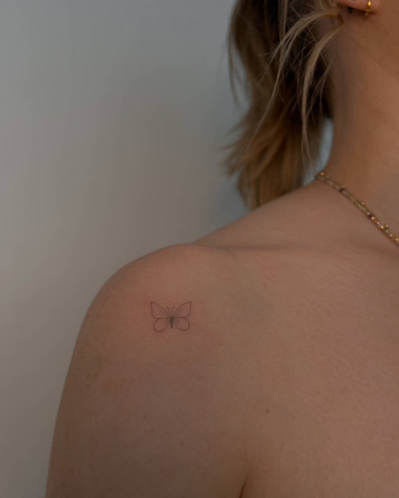 Little butterfly tattoo in fine line style located on the shoulder.