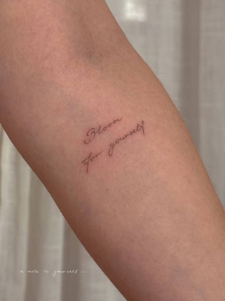 "Bloom for yourself" lettering tattoo handwritten on the inner forearm.
