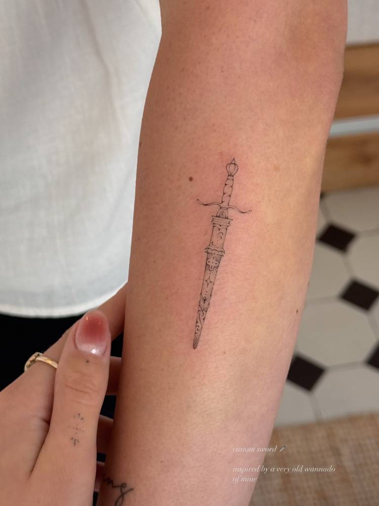 Dagger tattoo in fine line style done on the forearm.