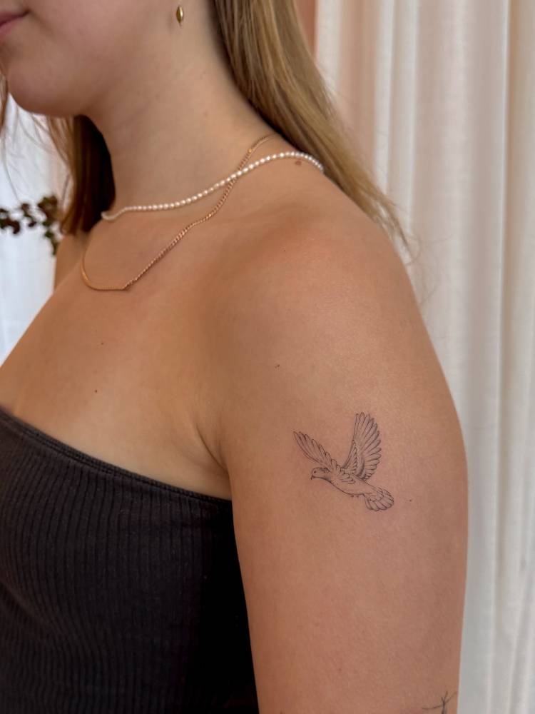 Dove tatoo located on the upper arm, fine line style.